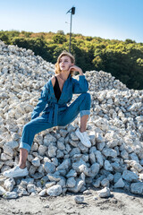 beautiful woman in blue overalls posing between large white rooted stones