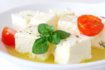 Feta cheese cubes with cherry tomato and olive oil in white bowl