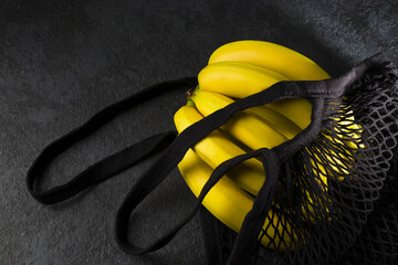 Yellow ripe bananas in a black eco-cotton string bag on a dark background. Reusable mesh shopping bag. Zero waste concept. Flat lay. Low key. View from above
