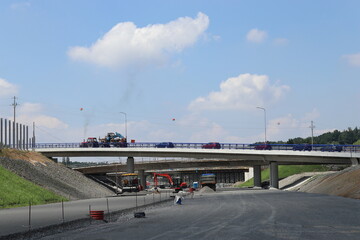 Construction of a new highway. A convoy of cars on a detour route. Bridge over the road.