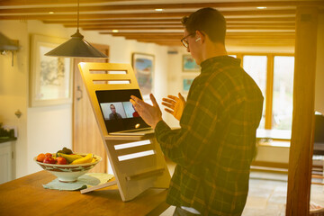Man video chatting with colleagues at laptop stand desk in kitchen
