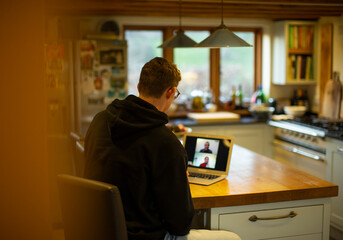 Man working at home video chatting with coworkers at laptop in kitchen