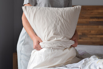 Woman is putting on pillow case while changing bed sheets