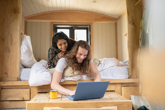 Happy young couple using laptop in tiny cabin bed - Powered by Adobe