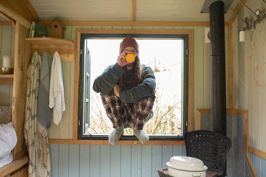 Young man in pajamas drinking coffee in tiny cabin window
