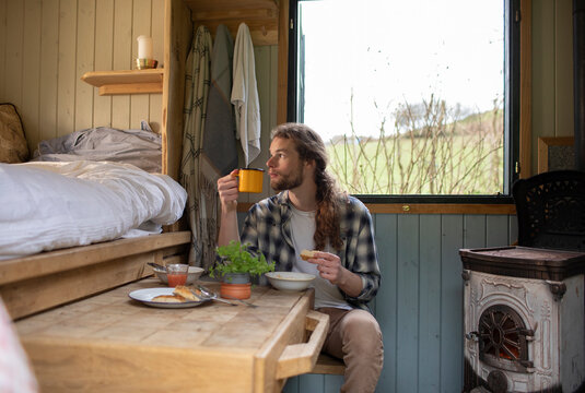 Young man eating and drinking in tiny cabin rental