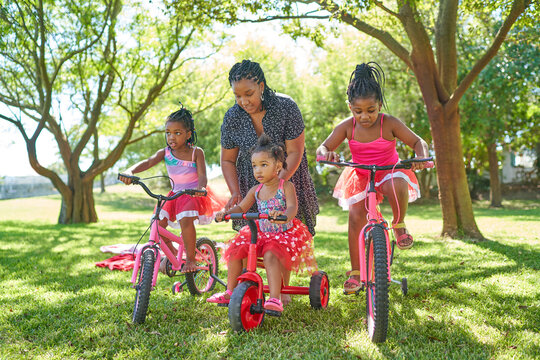 Mother and daughters with bicycles and tricycle in summer park