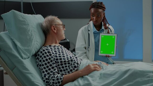Analysis doctor showing tablet with green screen to patient in hospital ward at medical recovery facility. African american specialist explaining old man about canner device consultation