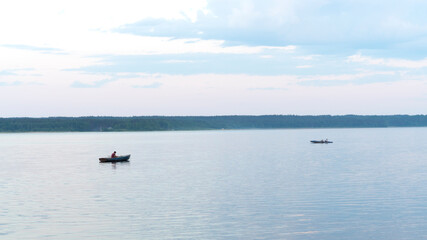 Fototapeta na wymiar A fisherman on his fishing boat on a calm river at sunset. Warm beautiful summer evening.