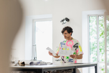 fashionable designer standing with sketches on blurred foreground