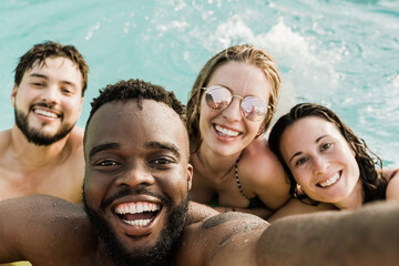 Multiracial friends at pool party taking a selfie with mobile phone - Millennials having fun during...