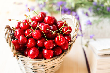 Harvest cherries in a basket on a wooden table with flowers and an open book. Seasonal red fruits. Diet food and healthy foods.