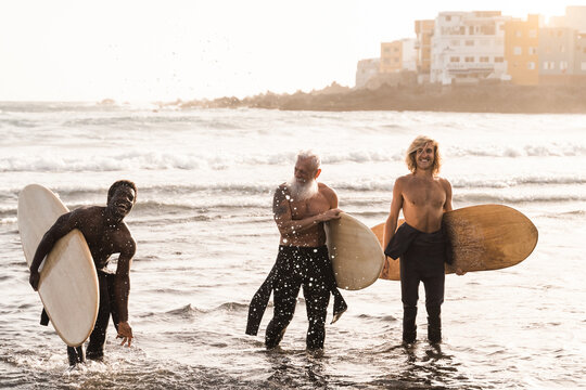 Multiracial surfer friends holding surf boards after extreme water sport session with beach on background -Soft focus on hipster senior man