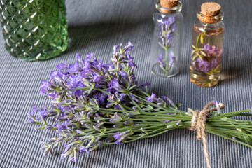 Obraz na płótnie Canvas A bunch of blooming lavender and small glass bottles with essential lavender oil and flowers on a gray background. Botanical cosmetics concept