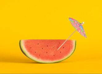 Fancy slice of ripe watermelon with cocktail  umbrella on yellow background.Copy space. Summer concept.