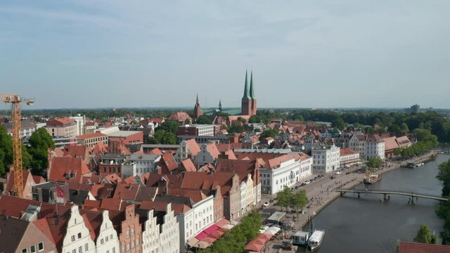 Forward fly towards Luebeck Dom, large brick cathedral. Aerial view of historic city centre. Tall buildings at riverside with decorative gables. Luebeck, Schleswig-Holstein, Germany