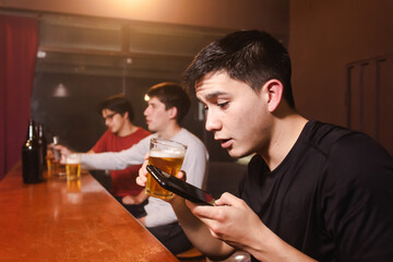 A young man sending a voice audio while having a beer with his friends at the bar.