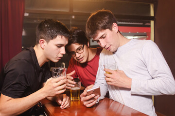 A group of friends watching a news item on the cell phone while drinking beer at the bar.