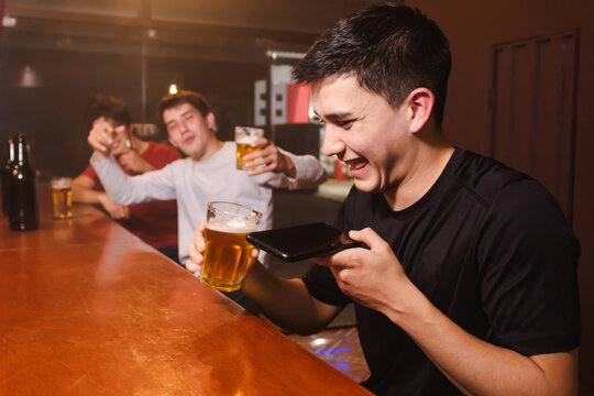 A young man laughing while sending a voice audio along with his drunken friends at the bar.