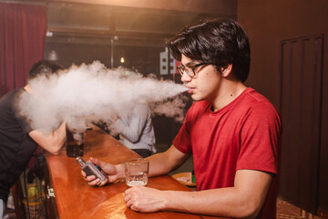 A young man blowing a cloud of vape smoke at the bar.