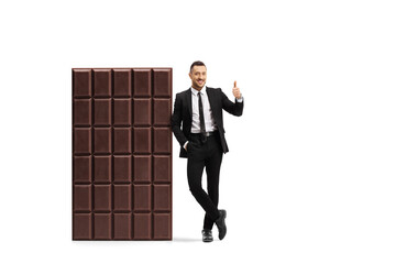 Full length portrait of a businessman leaning on a big chocolate bar and showing thumbs up