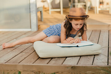 Mädchen sitzt auf Polster auf Holzterasse und liest ein Buch