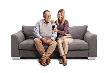 Elderly man and a young woman sitting on a sofa and looking at a mobile phone