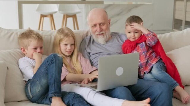 Happy family generations, elderly gray-haired grandfather with two grandchildren and granddaughter, communicate with relatives via video chat, webcam looking at laptop screen while sitting at home.