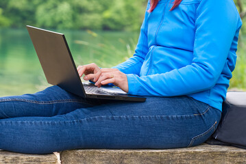 Naklejka premium Work from anywhere. Remote freelancer work in nature. Young woman, female freelancer working with laptop with Beautiful view of forest and lake. freelancer paradise, freedom of teleworking. distance
