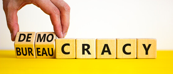 Democracy or bureaucracy symbol. Businessman turns wooden cubes and changes the word bureaucracy to democracy. Beautiful white background, copy space. Business and democracy or bureaucracy concept.