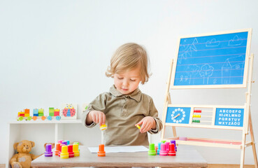 Cute little child having fun at home playing with colorful stamps on paper. Indoor activity for kids.