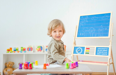 Cute little child having fun at home playing with colorful stamps on paper. Indoor activity for kids.