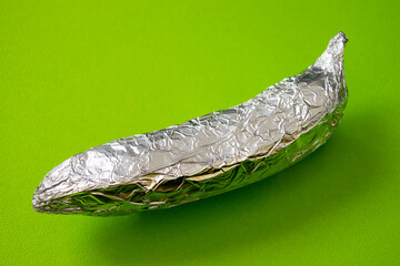 Banana covered with aluminum foil on a green background, irony of degradable bio packaging, nature...
