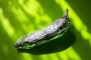 Banana covered with aluminum foil on a green background, irony of degradable bio packaging, nature manipulated by man.