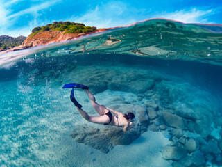 Half underwater view of a young woman diving deep into the sea water with mask and flippers. Amazing half underwater panorama. Cala Sinzias, Sardinia.