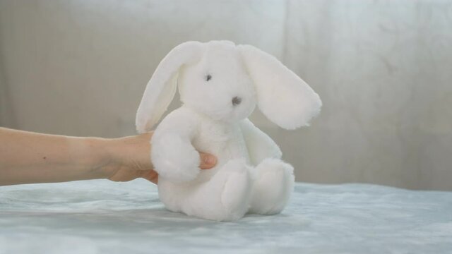 Toy rabbit fall on bed. Mom prepares present for her child and puts white plush rabbit. Mother preparing gift for baby for Easter or birthday. beautiful toy is placed in frame.