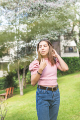 Outdoor portrait of a Latina teenage girl adjusting her straight hair with her hands in pink blouse and jeans