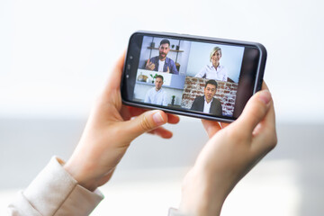 Video communication via smartphone. A young woman is using phone app for video call, online meeting. She talks with a several people together in same time. Close-up