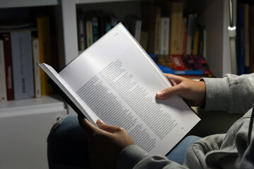 Cropped shot of a young Caucasian girl sitting in an armchair at home reading a book in the evening