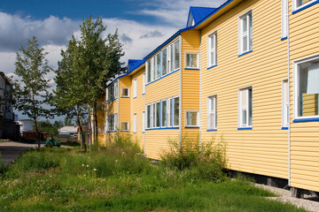 Fototapeta na wymiar Summer rural landscape. View of an apartment building. The walls are clad in yellow siding. Real estate in the countryside. Markovo village, Chukotka, Siberia, Far East of Russia.