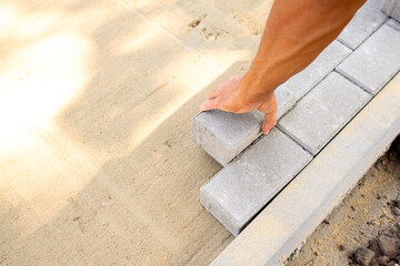 Bricklayer's hand lays paving slabs in prepared sand mixture. Process of laying sidewalk, landscaping garden