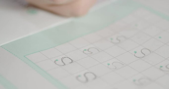 Close-up of a girl's hand learning alphabet writing the letter S on the school's book