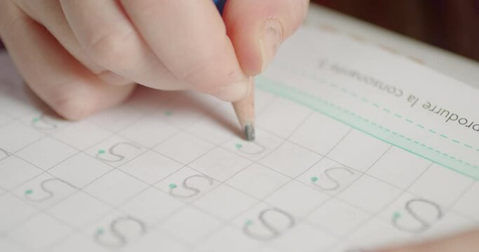 Close-up of a girl's hand learning alphabet writing the letter S on the school's book