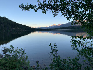 Tranquil view through trees of a mountain range and its reflection on a lake.