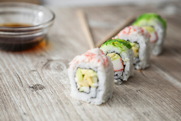 wooden texture with arranged sushi rolls next to bowl with soy sauce and chopsticks, healthy food and healthy lifestyle, studio