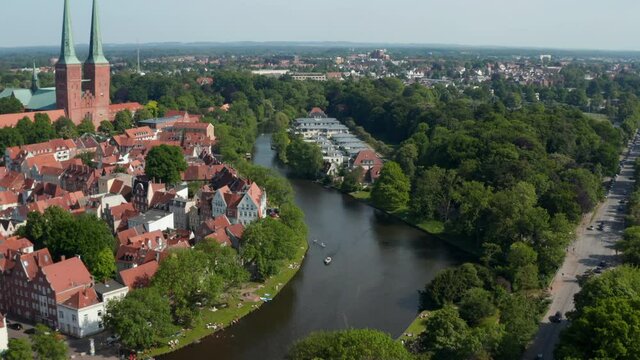 Tilt up reveal of Luebeck Cathedral, large brick-built Lutheran church. Forwards fly above Trave river flowing around historic city centre. Luebeck, Schleswig-Holstein, Germany