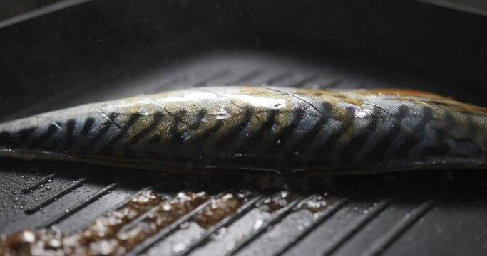 Close-up detail - Chef Cooking pours teriyaki sauce topped Saba fish grilled on a black hot pan, Japanese menu food cooking concept.
