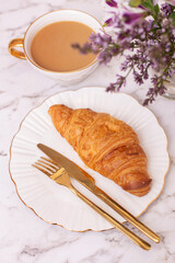 Coffee cup and sweet croissant on white table, decorated with beautiful flower bouquet