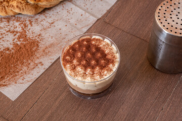 Italian tiramisu dessert inside a crystal glass sprinkled with cocoa on dark brown table