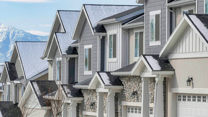 Pano Suburban homes with snowy roofs and white garage doors on a winter landscape